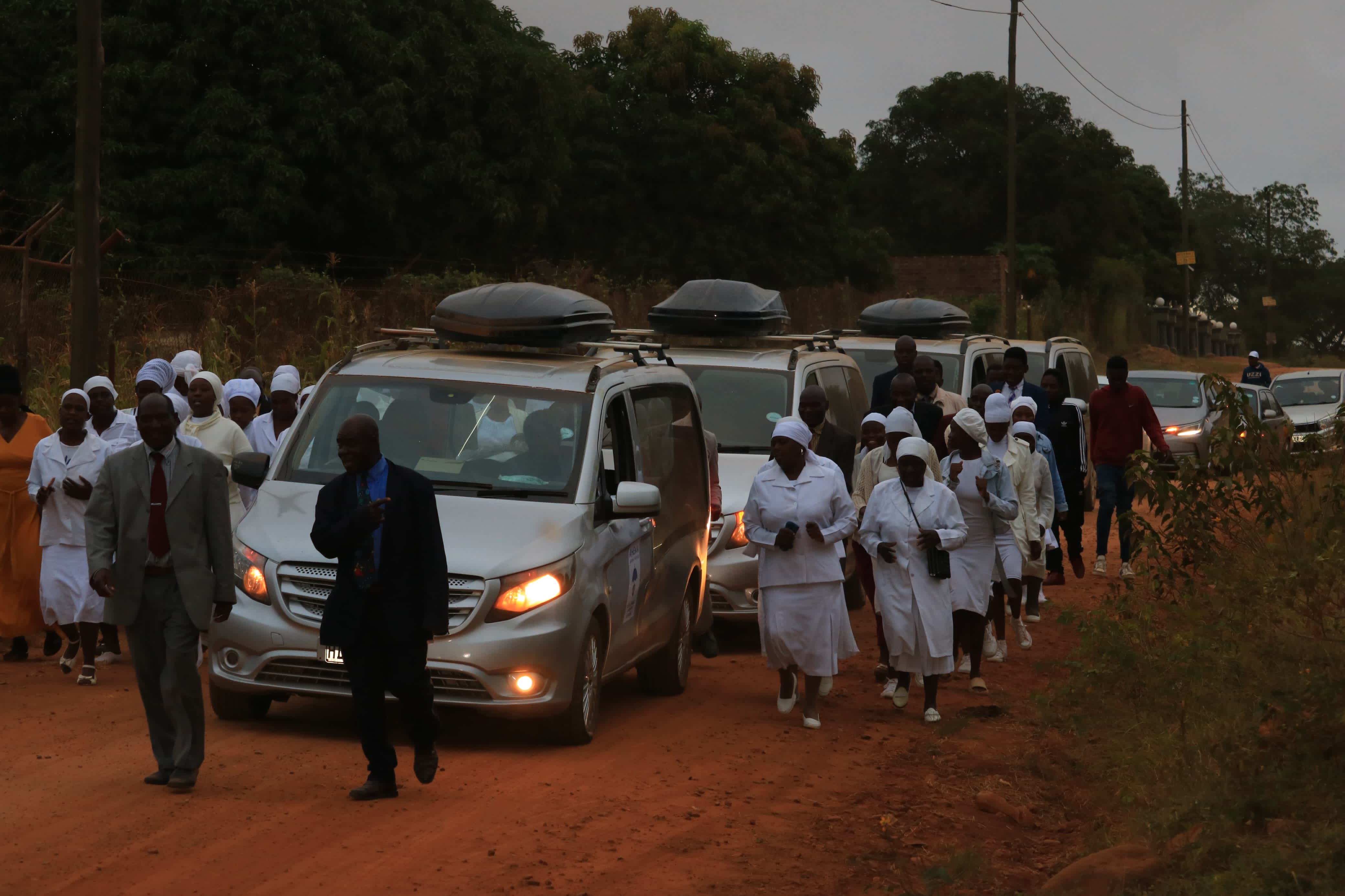 Funeral procession with support vehicles and attendees